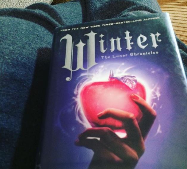 The book cover of Winter: a hand holding a glowing and seemingly magical red apple.