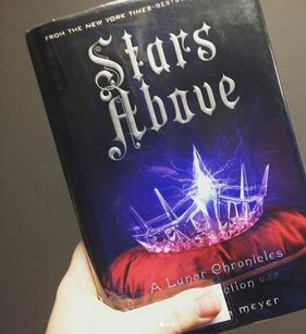 The book cover of Stars Above by Marissa Meyer shows a glowing glass crown atop a red pillow.
